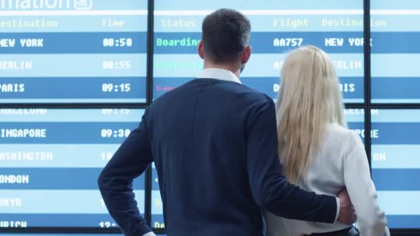 Kaukázusi etnikai férfi és a nő keresi a repülőtéren elhelyezett információs tábla. — Stock videók