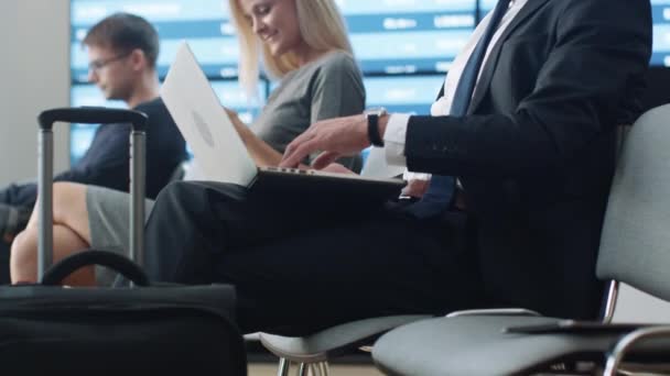 Geschäftsmann arbeitet am Laptop, während er in der Abflughalle am Flughafen auf sein Boarding wartet. — Stockvideo