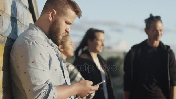 Genç adam kullanarak cep telefonu açık, onun genç arkadaşlar ayakta onun yanında grup. — Stok video