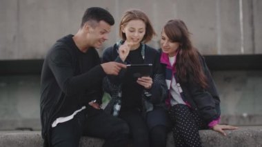 Grup gülen ve kentsel çevre mekanlarda eğlence için Tablet bilgisayarı kullanan gençler gülüyor.