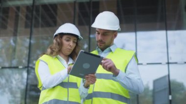 Adam ve kadın mühendisler var konuşma ve şantiye Tablet bilgisayar kullanıyor. Arka plan cam bina.