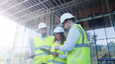 Üç konuşma ve Tablet bilgisayar kullanarak sahip şantiye mühendisleri takım. Arka plan cam bina.