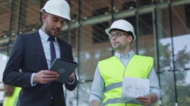 Mühendis ve işadamı baret yürüme, konuşma ve Tablet bilgisayar kullanarak. Cam binası veya gökdelen üzerinde arka plan yapım aşamasında.