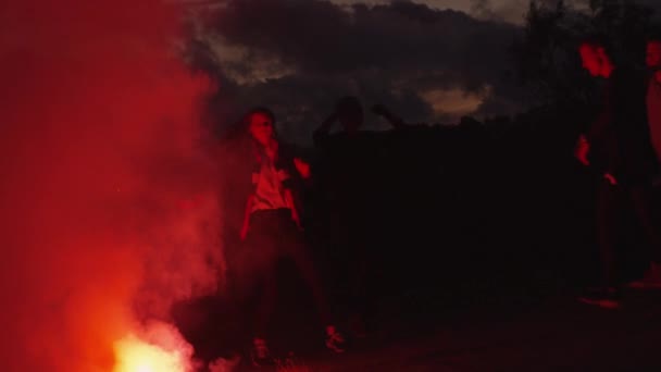 Grupo de adolescentes pasando el rato y bailando a la luz de la llamarada roja al aire libre . — Vídeo de stock