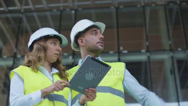 男人和女人的工程师有对话和在建筑工地上使用平板电脑。玻璃建筑背景. — 图库视频影像