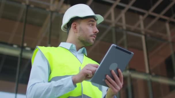 Mężczyzna inżynier przy użyciu komputera typu Tablet na placu budowy. Szkło budowlane na tle. — Wideo stockowe