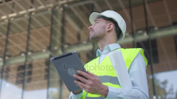 Mannelijke ingenieur met behulp van Tablet PC op de bouwplaats. Glazen gebouw op achtergrond. — Stockvideo