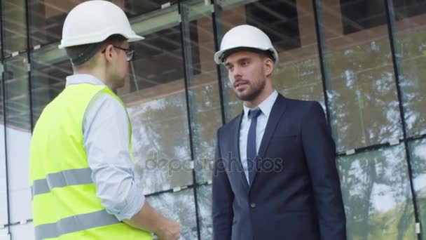 Zakenman en ingenieur in veiligheidshelmen overeenkomst Handshake gelet op bouwplaats. — Stockvideo