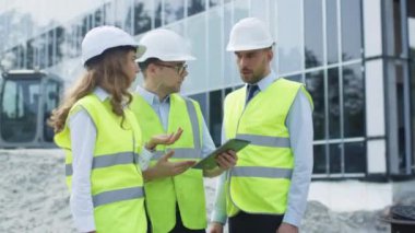 Grup üç konuşma ve Tablet bilgisayar kullanarak sahip mühendis. Cam bina yapım aşamasında zemin üzerine.