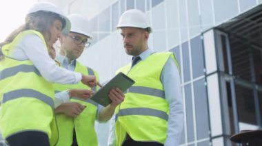 Grup üç konuşma ve Tablet bilgisayar kullanarak sahip mühendis. Cam bina yapım aşamasında zemin üzerine.