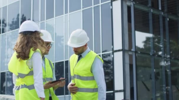 Team van drie ingenieurs met gesprek en met behulp van Tablet PC. Glazen gebouw in aanbouw op achtergrond. — Stockvideo