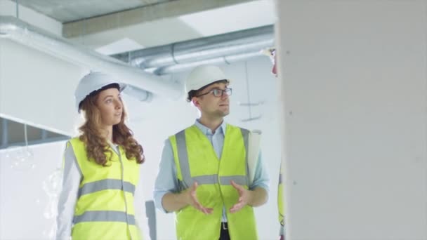 Csapat mérnökei a beszélgetést, látszó-on Blueprint, belső rész a épület építés alatt kemény kalap. — Stock videók