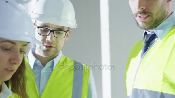 Zespół inżynierów w twardym kapelusze o rozmowy, patrząc na plan, wewnątrz budynku w trakcie budowy. — Wideo stockowe
