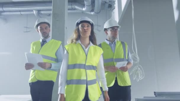 Equipe de engenheiros em chapéus duros andando e conversando, dentro do edifício sob construção . — Vídeo de Stock