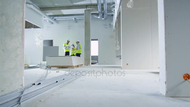 Team von Ingenieuren in harten Hüten im Gespräch, Blick auf den Bauplan, Gebäude im Bau. — Stockvideo