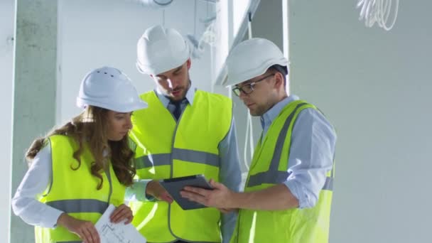 Equipe de engenheiros em chapéus duros tendo conversa, Olhando Tablet Computer, dentro do edifício em construção . — Vídeo de Stock