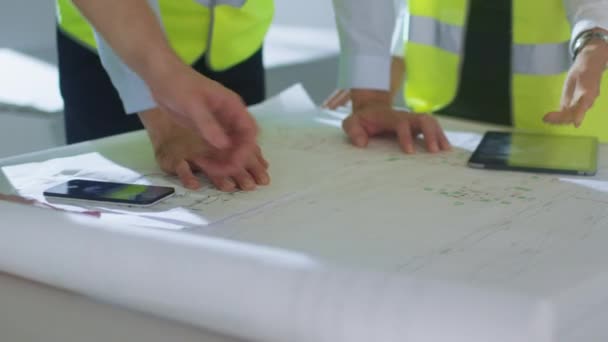Team av ingenjörer är bockning över stora plan och att ha samtal, inuti byggnaden Under Construction. — Stockvideo