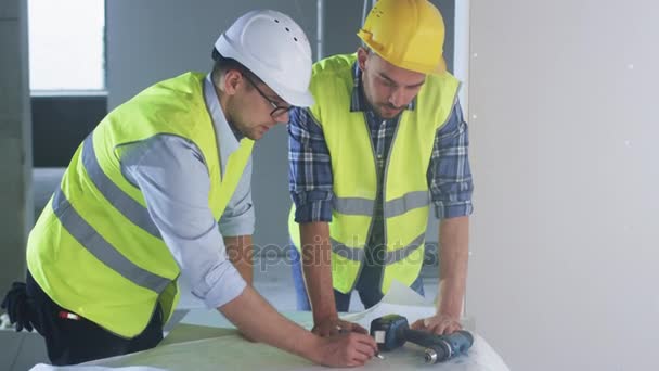 Engenheiro e trabalhador dobrando-se sobre grande Blueprint e tendo conversa, dentro do edifício em construção . — Vídeo de Stock