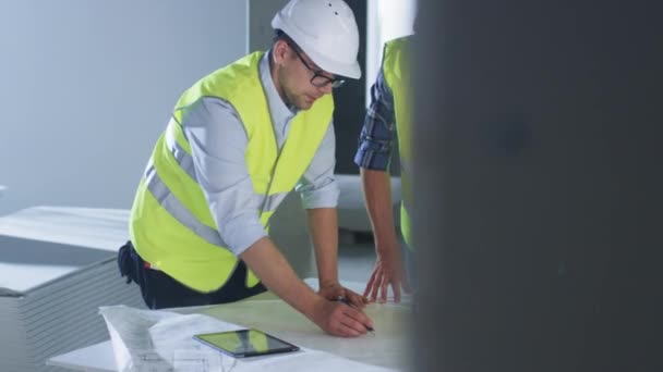 L'équipe d'ingénieurs se penche sur un grand plan directeur et discute, à l'intérieur du bâtiment en construction . — Video