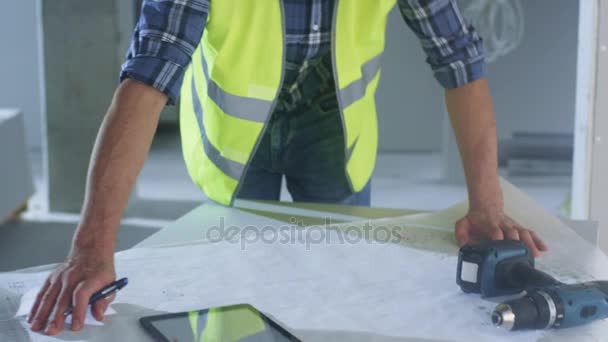 Stavební dělník v přilbu ohnou a při pohledu na svobodě Blueprint uvnitř budovy ve výstavbě. — Stock video