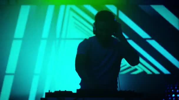 Ein beleuchteter DJ legt Musik in einem Nachtclub auf. Silhouette eines DJs. helle Animation auf Hintergrund.
