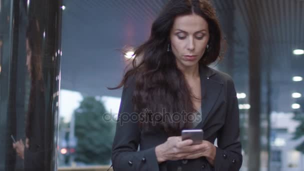 Mulher de negócios andando nas ruas do distrito de negócios segurando telefone móvel. Movimento lento — Vídeo de Stock