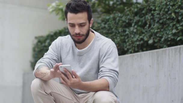 Jeune homme assis sur les marches à l'extérieur et utilisant le téléphone mobile. Environnement urbain moderne . — Video