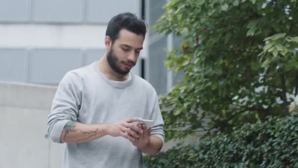Молодий чоловік сидить на сходах на відкритому повітрі і використовує мобільний телефон. Сучасне міське середовище . — стокове відео