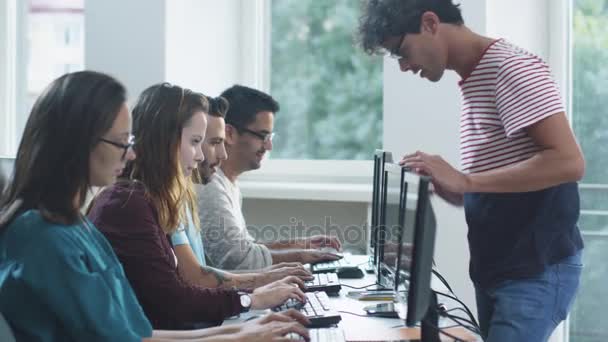 Grupo de Estudantes de Raça Mista estão sentados em fila e trabalhando em computadores, um jovem apontando para Monitor . — Vídeo de Stock