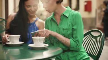 İki çekici genç kadın Giydir yaz ışık rahatla ve sokak kafede sohbet. Bir şey bir paylaşım diğer cep telefonu üzerinde heyecan verici.