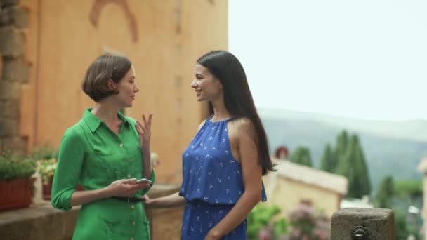 Twee aantrekkelijke jonge vrouwen in lichte zomer jurken hebben gesprek op straten van Europese stad. — Stockvideo