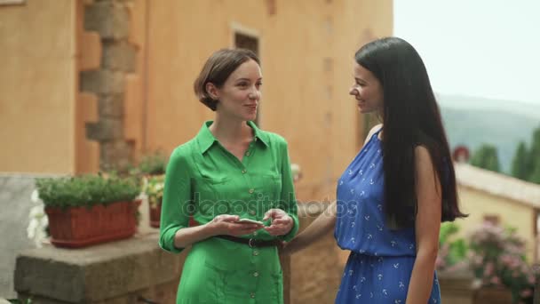 Zwei attraktive junge Frauen in hellen Sommerkleidern unterhalten sich auf den Straßen der europäischen Stadt. — Stockvideo