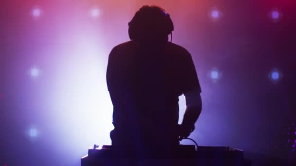 Ein beleuchteter DJ legt Musik in einem Nachtclub auf. Silhouette eines DJs — Stockvideo