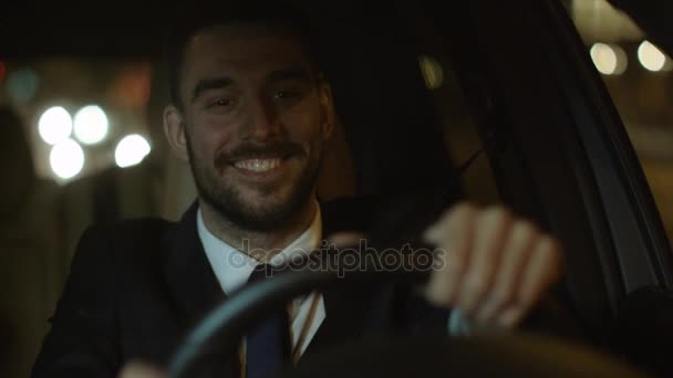 Feliz hombre de negocios sonriente conduciendo un coche a través de las calles de la ciudad nocturna . — Vídeos de Stock