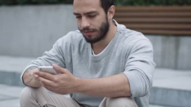 Adımları açık havada üzerinde oturan ve cep telefonuyla genç adam.