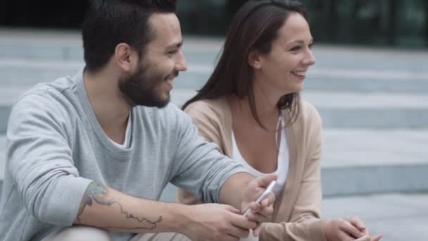 Jeune homme et femme heureux et souriants sont assis sur les marches à l'extérieur et communiquant . — Video