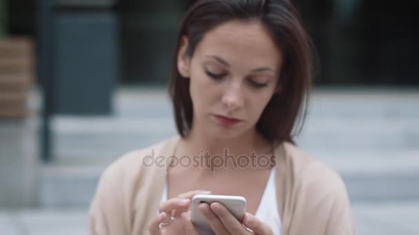 Jonge aantrekkelijke vrouw met behulp van de mobiele telefoon buitenshuis. — Stockvideo