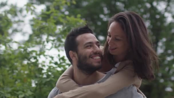 Riendo y sonriendo pareja divirtiéndose al aire libre. hombre dando chica piggyback paseo . — Vídeos de Stock