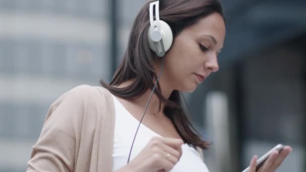 Junge attraktive Frau, die auf der Straße läuft und Musik hört. modernes städtisches Umfeld. — Stockvideo