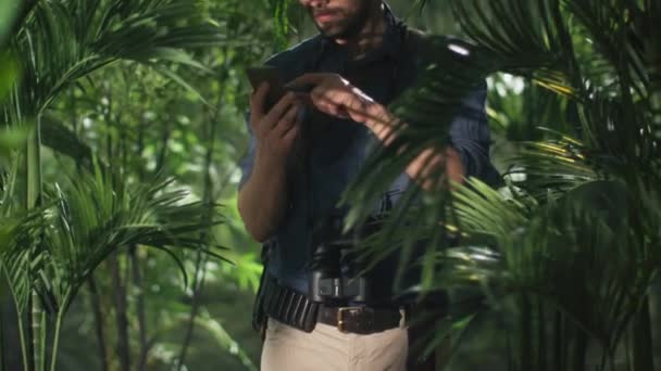 Aventurier en chapeau en utilisant le téléphone portable dans la forêt de jungle . — Video