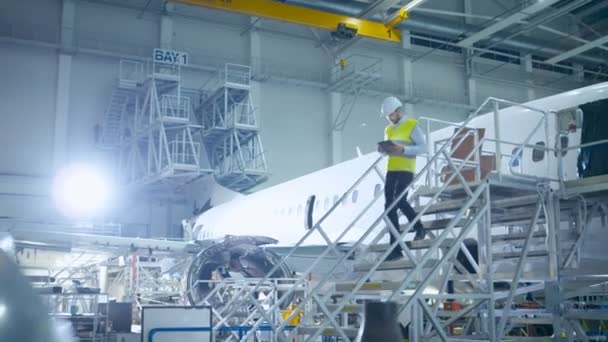 Ingeniero de aviones en chaleco de seguridad caminando a través del hangar de mantenimiento de aeronaves — Vídeo de stock