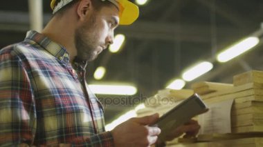 İşçi ahşap stok bir kereste fabrikası depoda bir tablet bilgisayar kullanarak sayar.