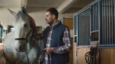 Adam beyaz bir at bir ahırda okşayarak.