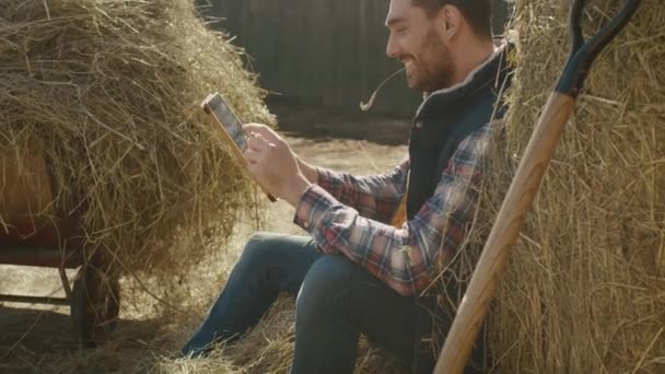 男が干し草で座っていると、タブレット コンピューターを使用して. — ストック動画