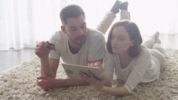 Мужчина и женщина лежат на полу и используют планшет для покупок в Интернете . — стоковое видео