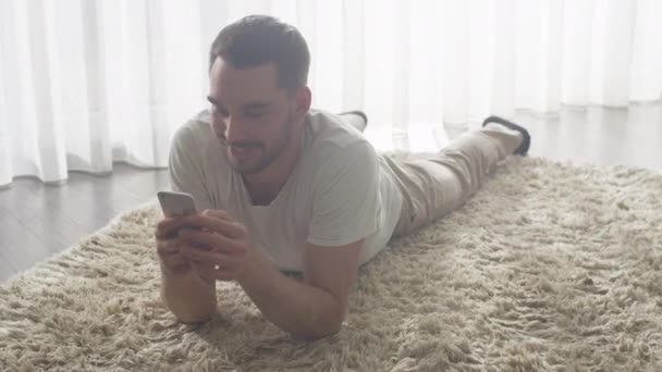Człowiek leżący na podłodze w salonie i przy użyciu telefonu komórkowego dla rozrywki. — Wideo stockowe