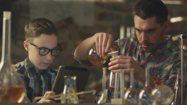 Apa és fia, hogy kémiai kísérletekhez, egy tabletta számítógép, egy garázs otthon ellenőrzése közben. — Stock videók