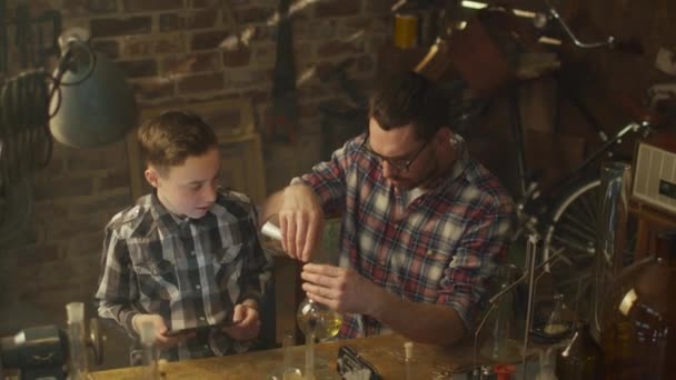 Otec a syn dělají chemické pokusy při kontrole tabletový počítač v garáži doma. — Stock video