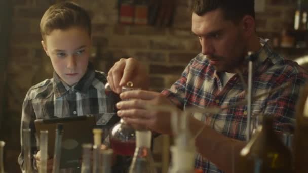 Πατέρας και γιος κάνουν πειράματα χημείας ενώ ελέγχετε έναν υπολογιστή tablet σε ένα γκαράζ στο σπίτι. — Αρχείο Βίντεο