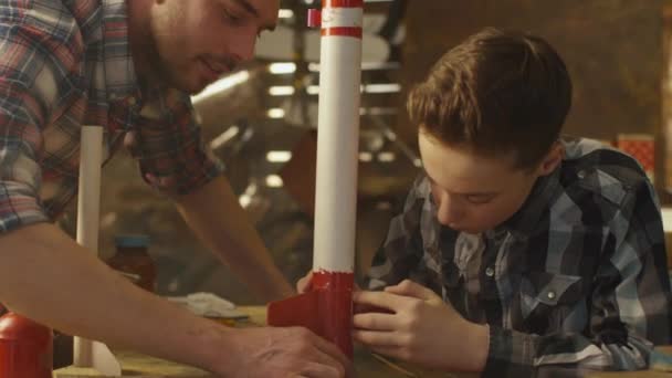Πατέρας και γιος μοντελοποίηση έναν πύραυλο παιχνιδιών σε ένα γκαράζ στο σπίτι. — Αρχείο Βίντεο